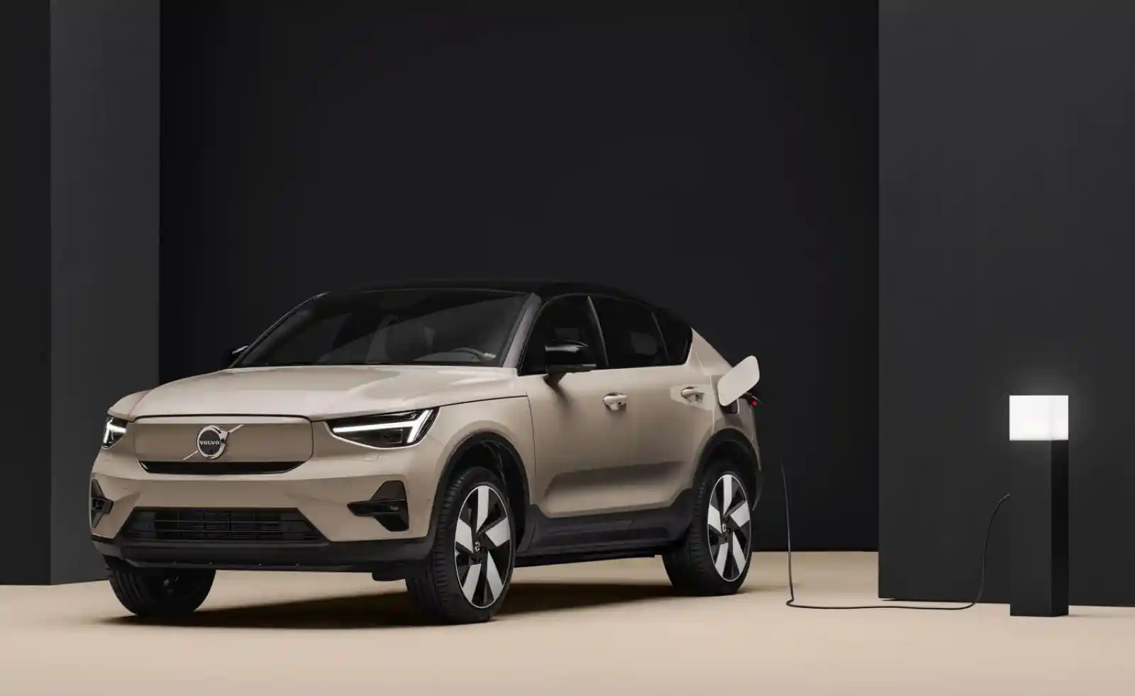 볼보 EX30 전기 SUV 충전 중 측면 이미지, 베이지 컬러 차체와 충전 케이블이 연결된 모습