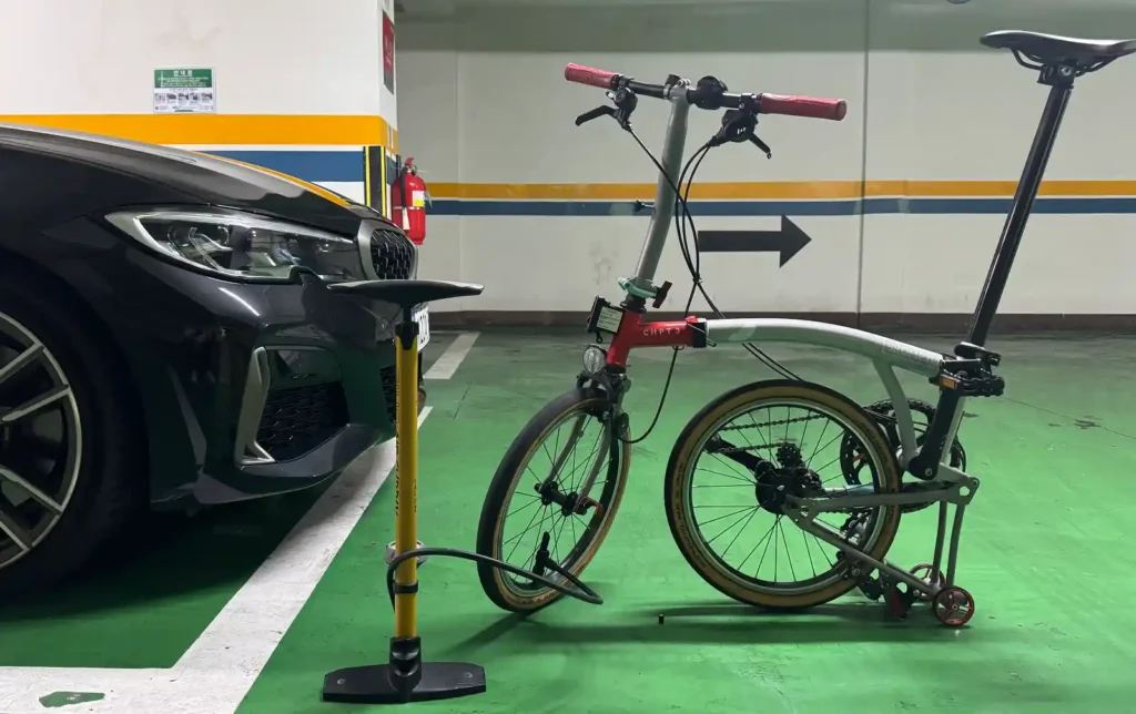 주차장에서 브롬톤 자전거의 타이어에 손펌프로 공기압을 보충하는 장면, 실제 사용 환경에서 진행되는 공기압 점검 모습