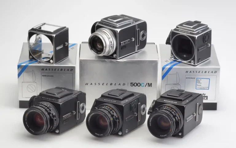 핫셀블라드 500C/M 중형 필름 카메라 6대가 원본 박스와 함께 배치된 모습. 상단에는 바디, 필름 백, 파인더가 분리된 상태로 전시되어 있고 하단에는 칼 자이스 렌즈가 장착된 완성 상태의 카메라 3대가 놓여 있어 V 시스템의 모듀러 구조를 한눈에 보여주는 이미지