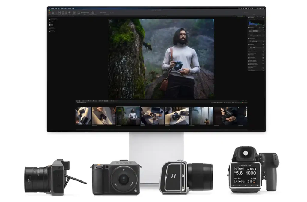 핫셀블라드 Phocus 소프트웨어가 실행된 대형 모니터와 그 아래 배치된 핫셀블라드 X 시스템 카메라 4대. 모니터 화면에는 산악 풍경 속 인물 사진 편집 화면이 표시되어 있으며, 하단 필름스트립에는 여러 썸네일이 보임. HNCS RAW 편집 워크플로우의 전체 시스템을 보여주는 이미지