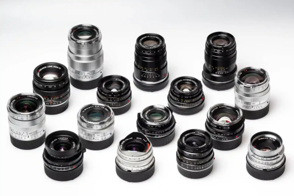 다양한 세대의 라이카 M 렌즈 컬렉션. 1980년대 이전 구형 렌즈와 2000년대 이후 현행 렌즈가 섞여 있으며, 블랙 크롬과 실버 크롬 마감의 광각부터 망원까지 총 15개 렌즈가 흰 배경 위에 배치되어 있음