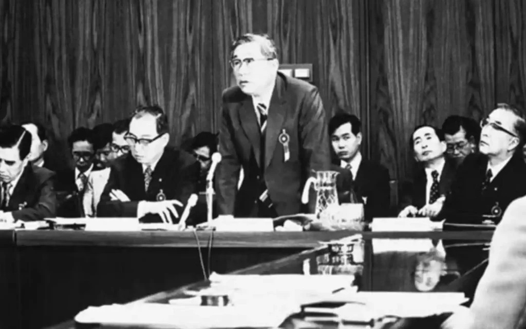 1980년대 토요타 경영진 회의 장면, 한 임원이 서서 발언하고 있으며 여러 경영진이 테이블에 앉아 경청하고 있다