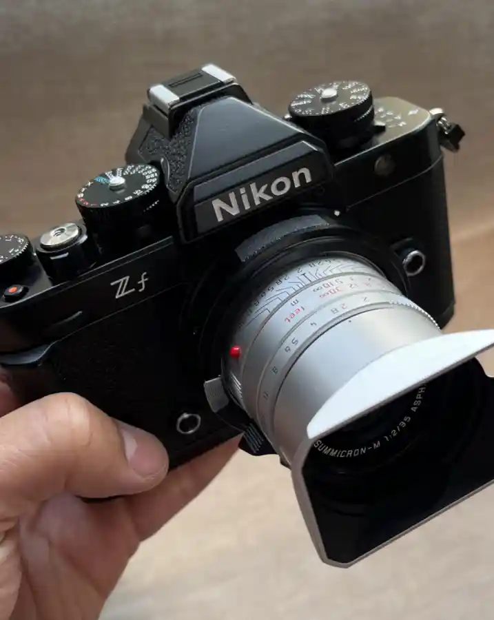 어댑터를 활용해 니콘 Zf 미러리스 카메라에 은색 라이카 M 마운트 렌즈를 장착하고 손으로 든 모습