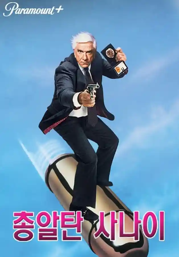 영화 '총알탄 사나이(The Naked Gun)' 한국 공식 포스터. 주인공 프랭크 드레빈(레슬리 닐슨)이 검은 정장을 입고 총과 배지를 들고 거대한 총알 위에 올라타 있는 코믹한 장면. 파란 하늘 배경에 상단에 'Paramount+' 로고, 하단에 분홍색으로 '총알탄 사나이'라는 한글 제목이 적혀 있다.