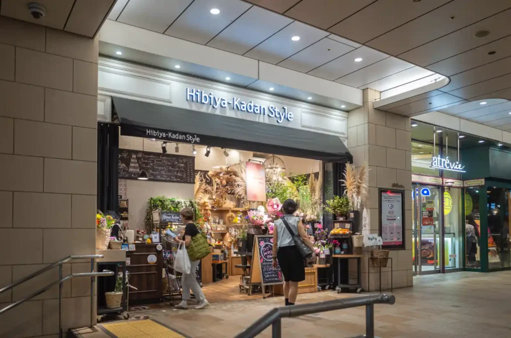 오츠카역 인근 히비야 카단 스타일(Hibiya-Kadan Style) 꽃집 야경. 다양한 꽃과 화분, 드라이플라워가 진열되어 있고, 두 명의 손님이 꽃을 구경하고 있는 모습