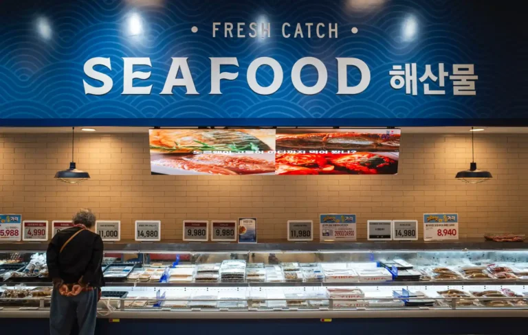 이마트 푸드마켓 수산 코너에서 리코 GR2로 촬영한 사진. FRESH CATCH SEAFOOD 간판 아래 냉장 진열대 앞에서 수산물을 고르는 고객의 모습. 파란색 톤의 간판과 따뜻한 조명이 대비를 이루며, 진열대에는 각종 수산물과 가격표가 빼곡하게 배치되어 있다.