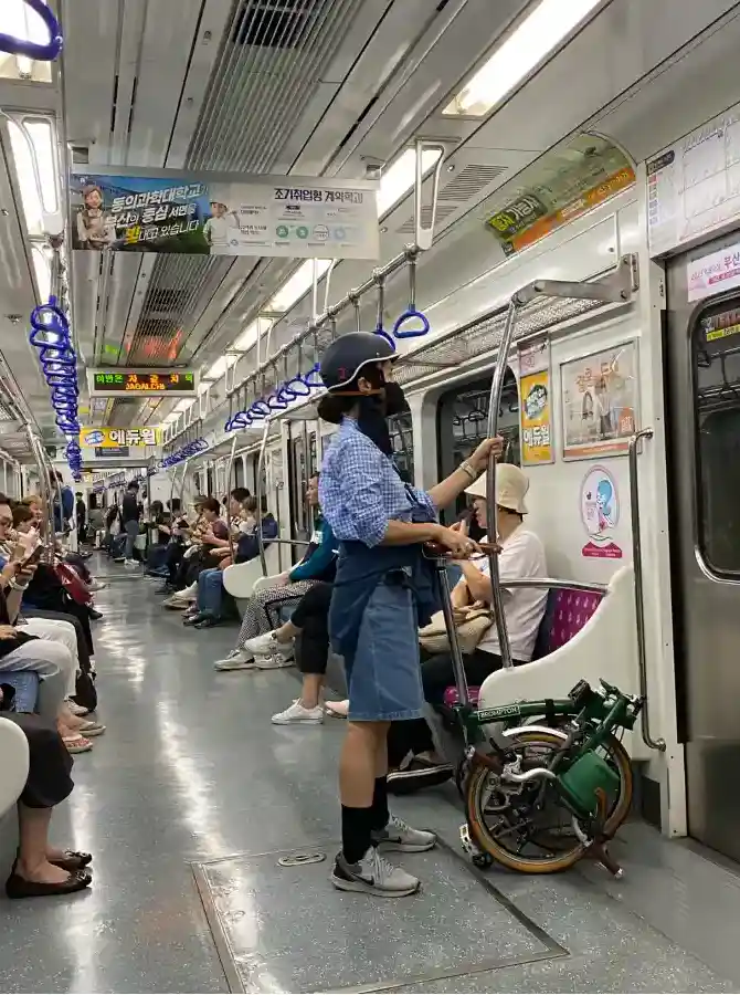 부산 지하철 객차 안에서 접힌 브롬톤을 휴대하고 손잡이를 잡고 서 있는 라이더의 모습