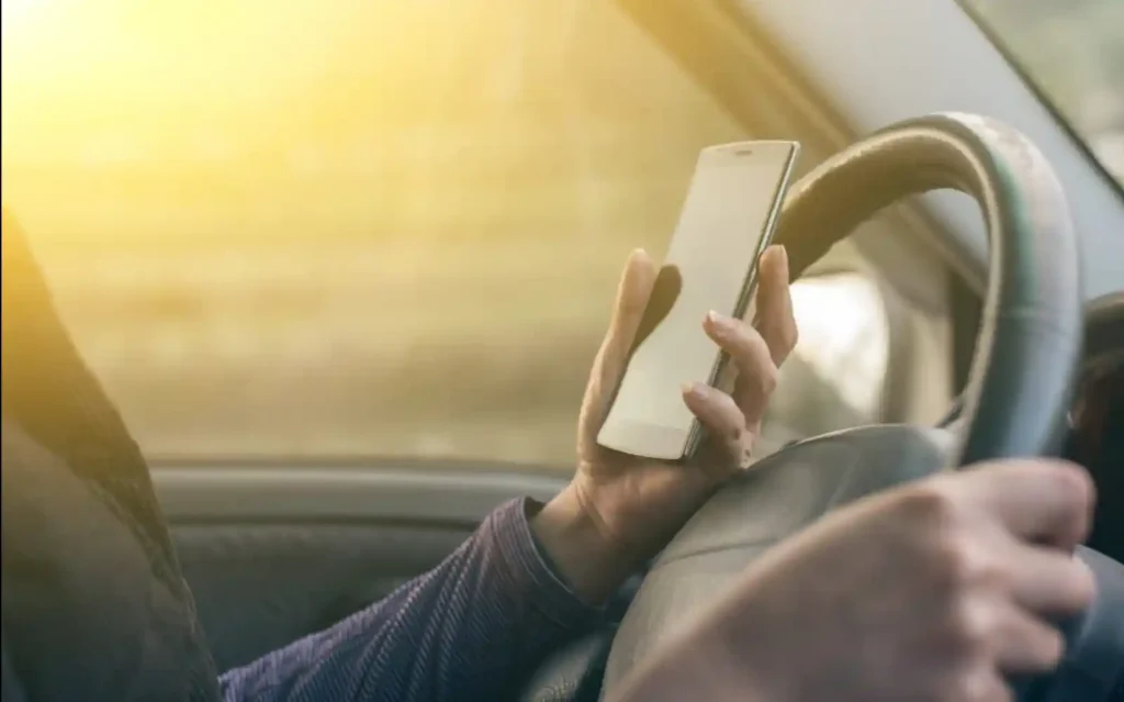 운전 중 스마트폰 조작 모습 - 핸들 잡은 채 휴대폰 보는 운전자 손 클로즈업