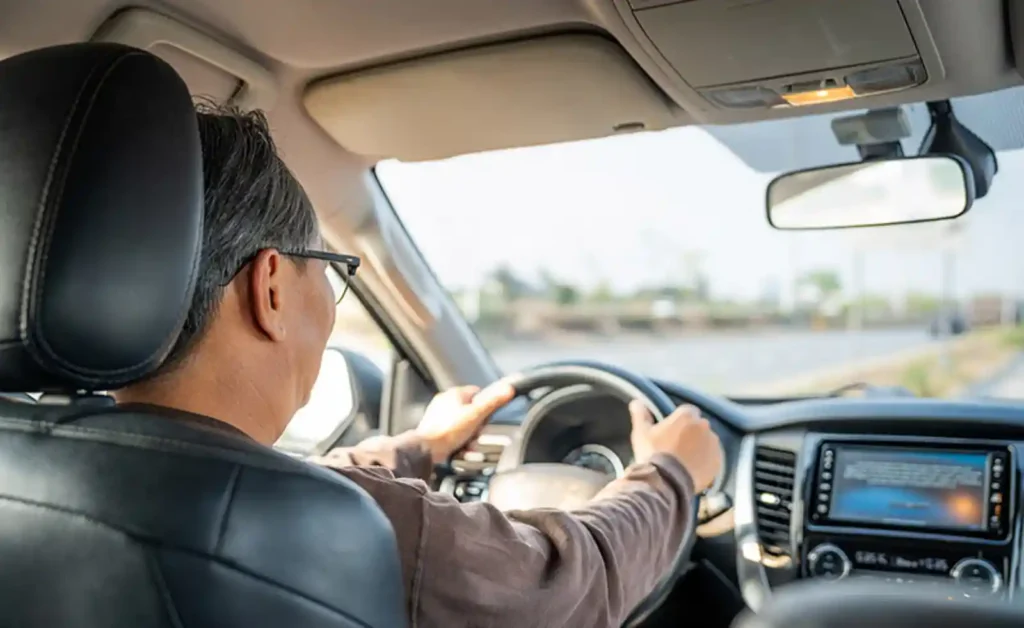 고령 운전자가 운전석에서 핸들을 잡고 전방을 주시하며 운전하는 뒷모습 - 조건부 면허제