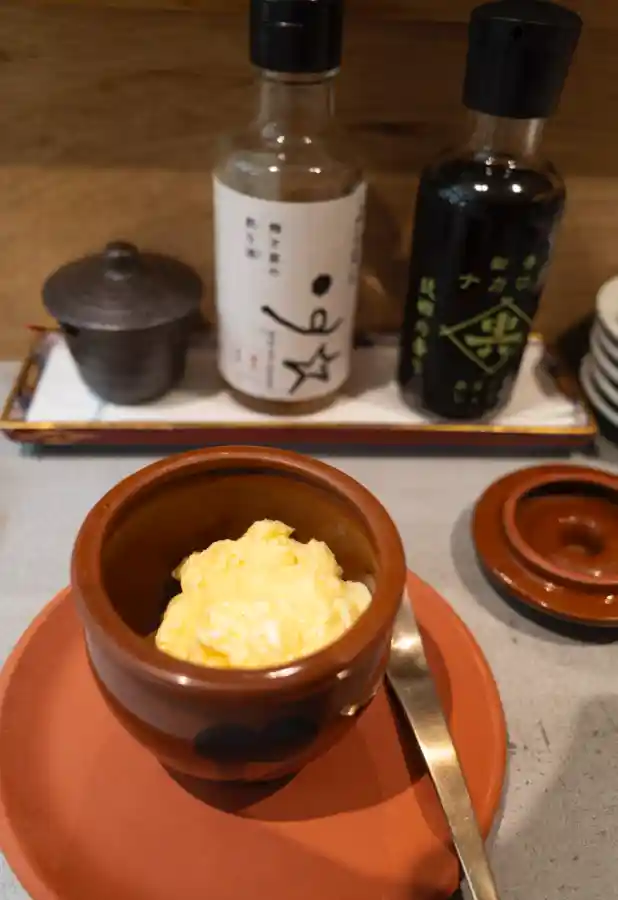 우메토호시 차완무시(일본식 계란찜). 갈색 도자기 그릇에 부들부들한 노란색 계란찜이 담겨 있고, 뒤편으로 우메토호시 로고가 새겨진 간장병과 조미료들이 보인다.