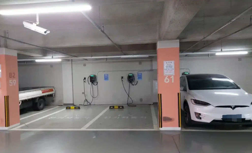아파트 지하주차장 전기차 완속충전기 설치 모습, 벽면에 부착된 충전기 여러 대와 충전 중인 테슬라 모델X