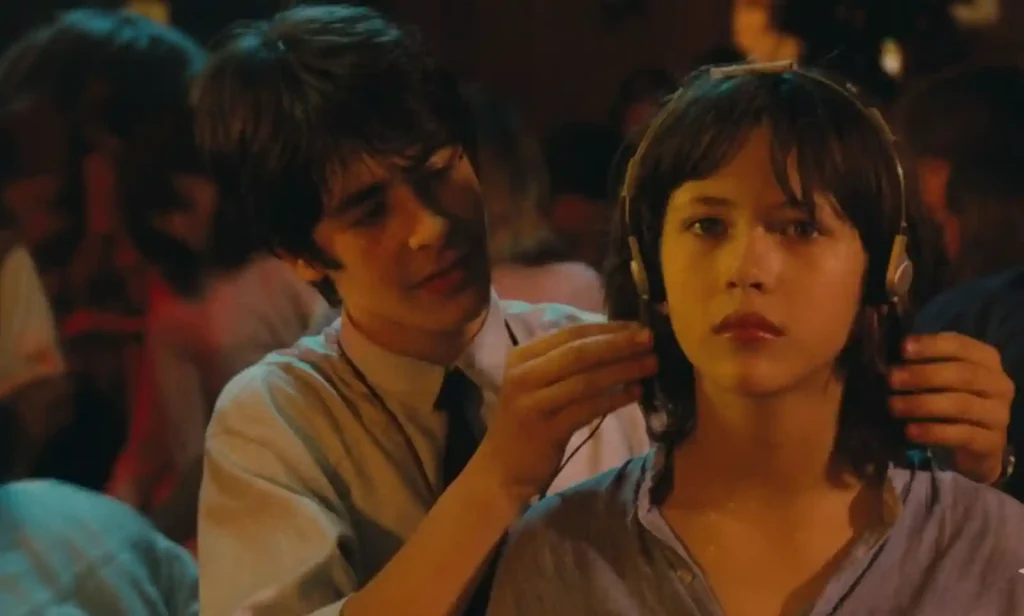 영화 '유 콜 잇 러브'의 한 장면. 한 남자가 여주인공인 소피 마르소에게 헤드폰을 끼워주고 있다. 따뜻한 조명의 실내 배경.