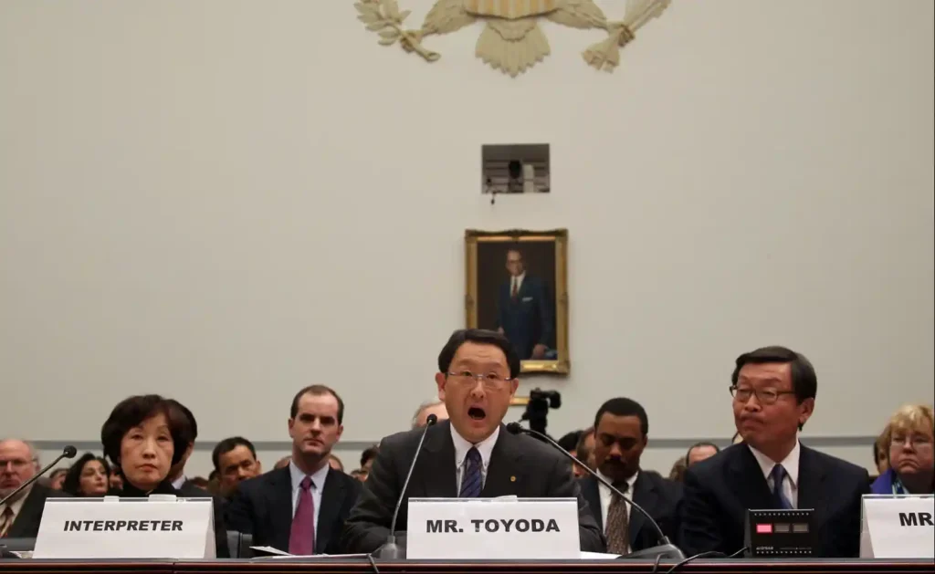 2010년 미국 하원 청문회에서 증언하는 도요다 아키오, MR TOYODA 명패 앞에서 진지한 표정으로 마이크에 대고 말하는 모습