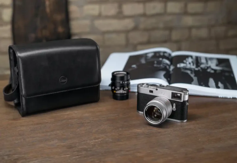 라이카 M 카메라 실버 크롬 바디와 렌즈 2개, 가죽 케이스가 나무 테이블 위에 놓여있는 모습