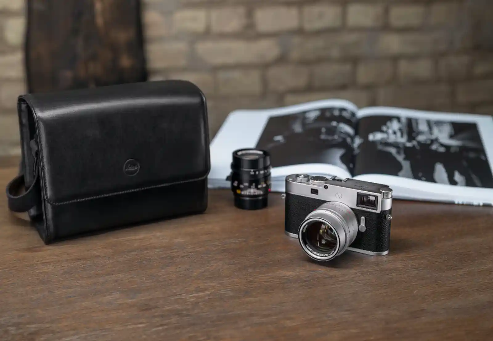 라이카 M 카메라 실버 크롬 바디와 렌즈 2개, 가죽 케이스가 나무 테이블 위에 놓여있는 모습