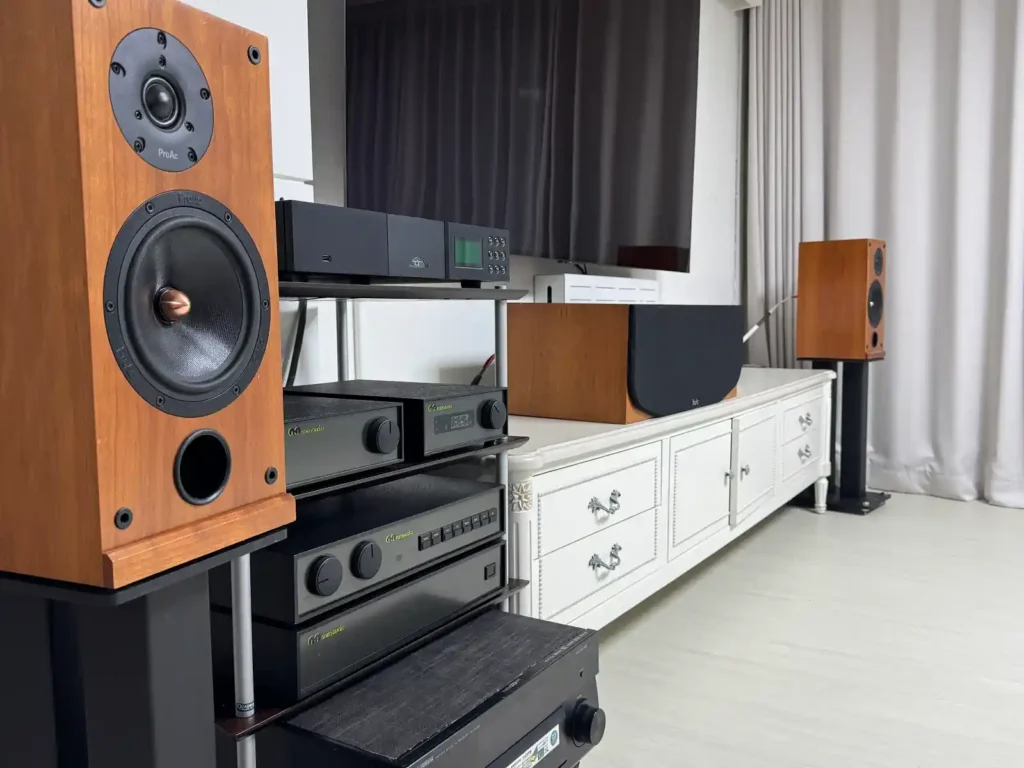 프로악 Response D2 스피커와 네임 오디오 시스템 구성, 왼쪽에 프로악 D2 프런트 스피커, 중앙 랙에 NAC 102 NAP 180 앰프와 NDX 네트워크 플레이어, 오른쪽에 프로악 CC2 센터 스피커