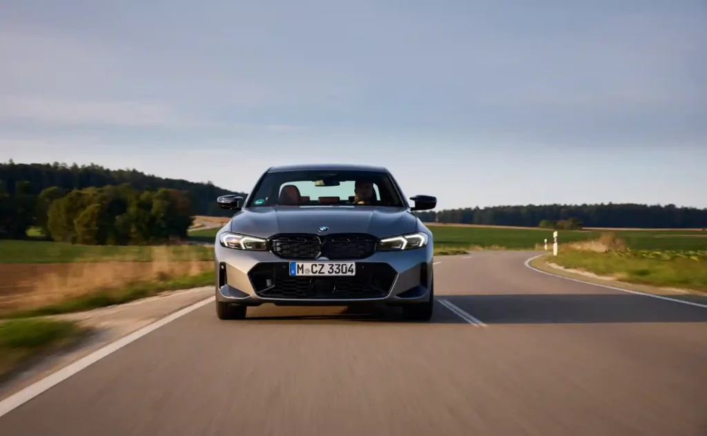 BMW M340i가 컨트리 로드를 주행하는 정면 모습 - 키드니 그릴과 헤드램프가 강조된 역동적인 장면