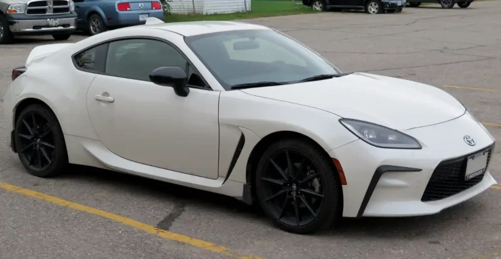 주차장에 세워진 흰색 Toyota 86 스포츠 쿠페. 검은색 휠과 에어로 파츠가 장착된 2도어 차량으로, 과거 Scion FR-S였던 모델이 Toyota 브랜드로 재탄생한 모습