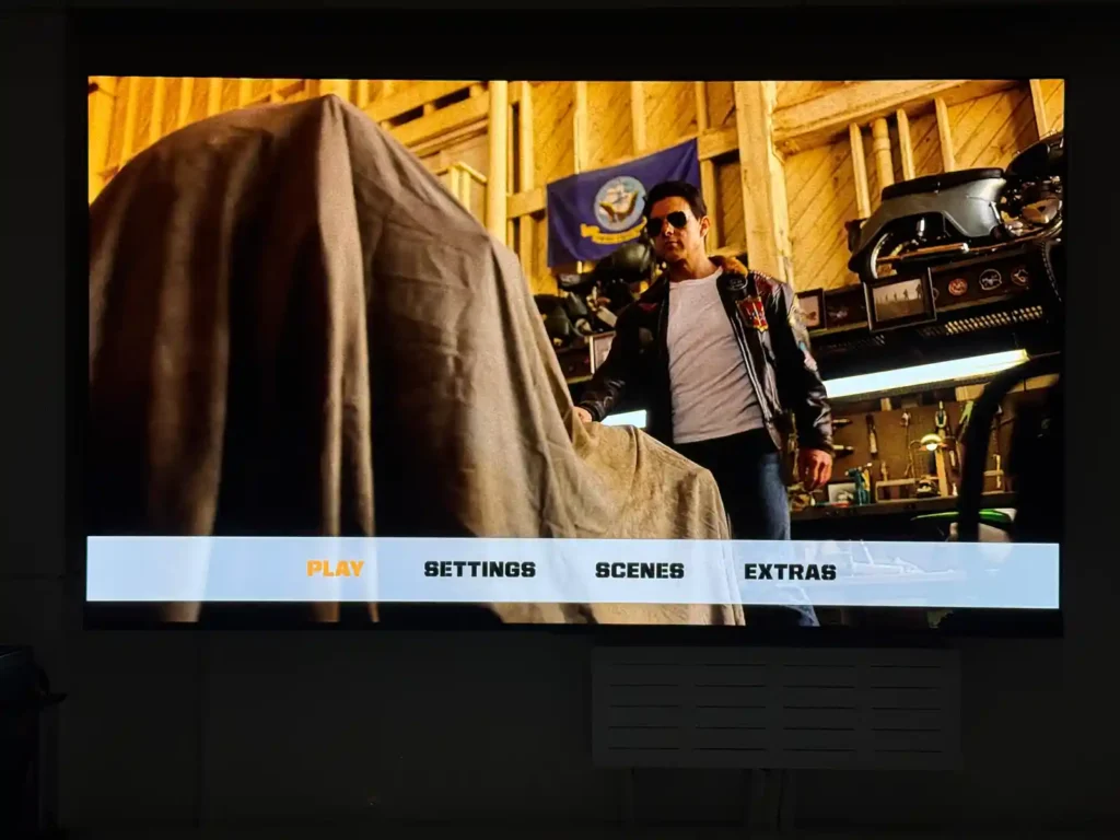 대형 TV 화면에 표시된 블루레이 메뉴 화면, PLAY SETTINGS SCENES EXTRAS 옵션이 보이는 영화 감상 준비 단계