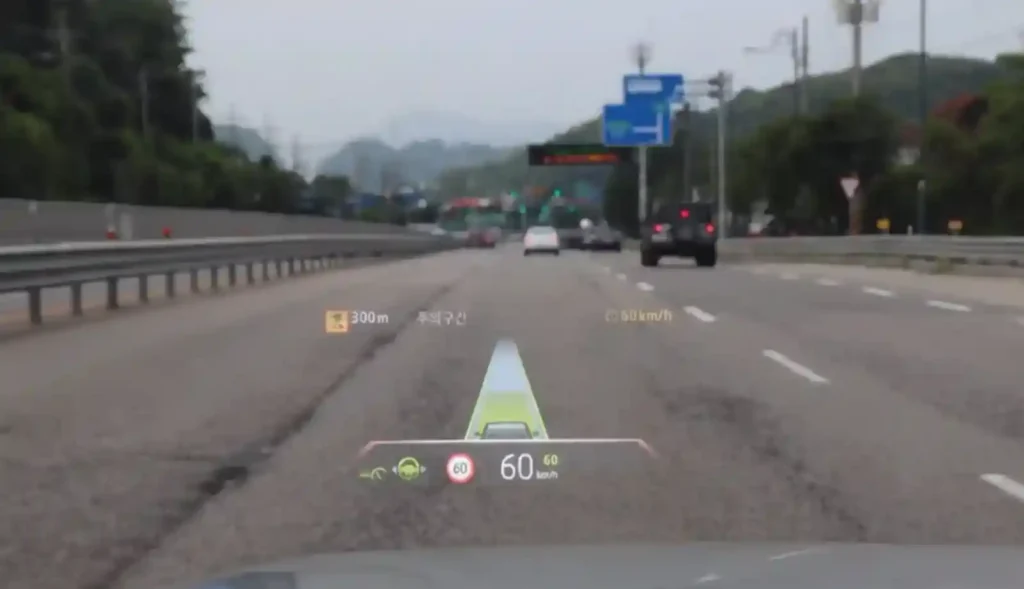 BMW 차량 주행 중 전면 유리에 표시된 HUD 화면으로, 속도와 내비게이션 정보가 실제 도로 위에 겹쳐 보이는 모습