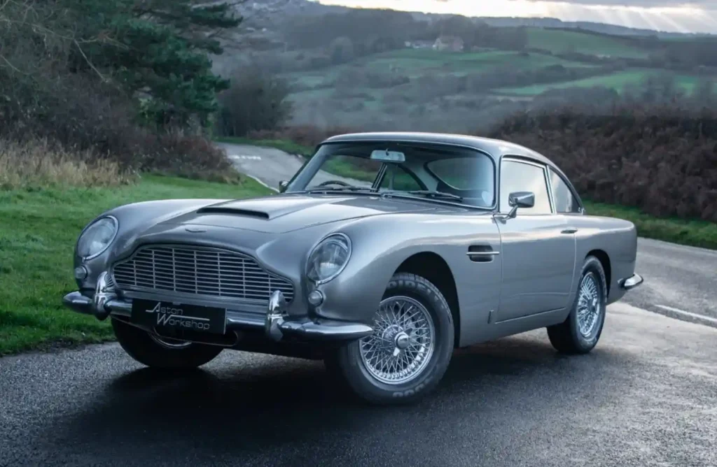 야외 도로에 정차해 있는 클래식 애스턴 마틴 DB5의 정면 3/4 모습