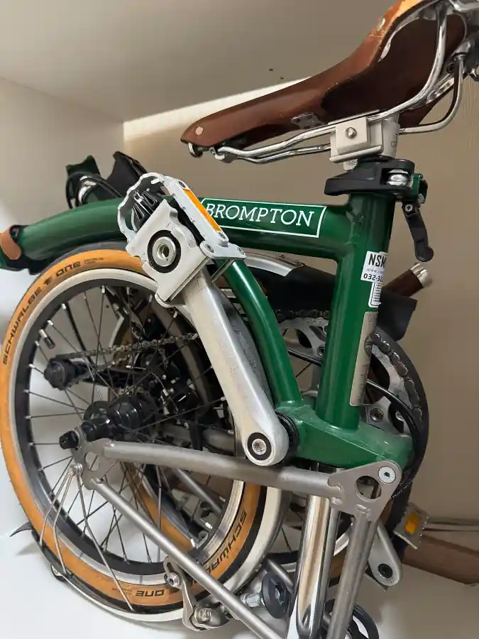 실내에 접어서 보관 중인 브롬톤 M4L. 레이싱 그린 프레임에 브라운 가죽 안장과 탄 색상 슈발베 타이어가 특징적이다.