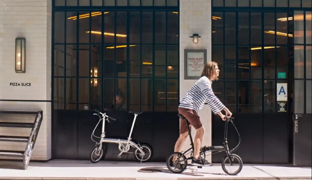 도심 거리에서 다혼 폴딩 자전거를 타는 모습, 카페 앞을 지나가는 라이딩 장면