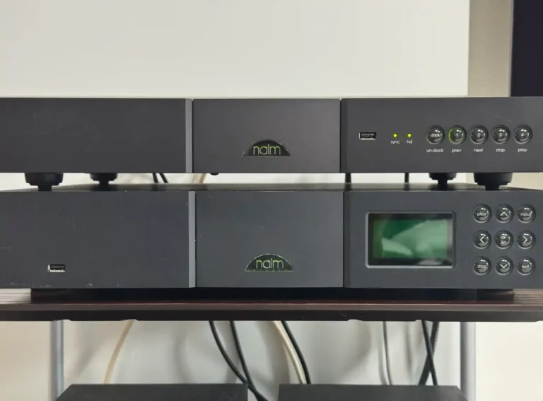 네임 nDAC와 NDX가 나란히 놓인 오디오 시스템. 위쪽 nDAC는 깔끔한 전면부와 조작 버튼이 보이고, 아래쪽 NDX는 전원이 켜져 초록색 naim 로고는 빛나지만 전면 디스플레이 화면은 꺼진 상태다.