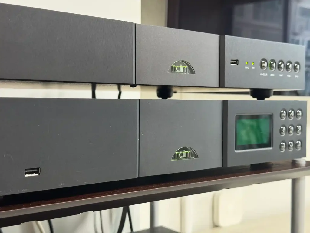 네임 nDAC와 NDX가 상하로 놓인 모습. 위쪽 nDAC는 초록색 로고가 빛나고 있고, 아래쪽 NDX는 로고는 빛나지만 전면 디스플레이 화면이 완전히 꺼져 검게 보인다.