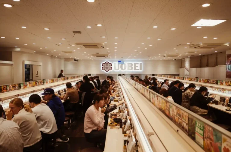 시부야 우오베이 회전초밥 매장 내부 전경, 일렬로 배치된 좌석에서 식사 중인 손님들과 UOBEI 로고