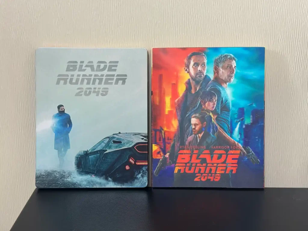 블레이드 러너 2049 스틸북 - 화려한 네온 컬러의 아웃 케이스와 미니멀한 청회색 메탈 스틸북 케이스 비교