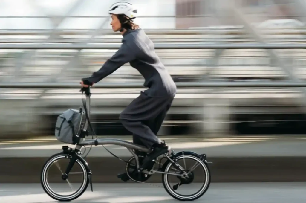 브롬톤 전기자전거를 타고 도심 다리 위를 주행 중인 여성 라이더 — e-Motiq 어댑티브 인텔리전스 실사용 장면