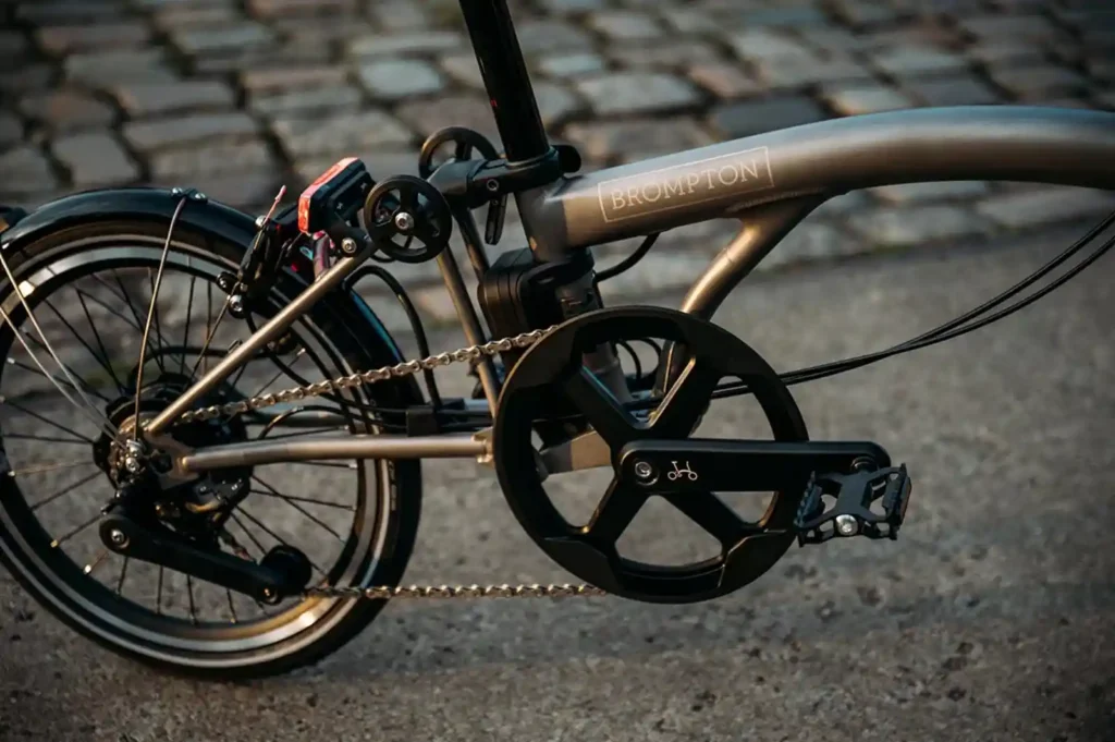 브롬톤 Electric T Line 티타늄 프레임 드라이브트레인 클로즈업 — BROMPTON 각인 로고와 체인, 크랭크셋 디테일