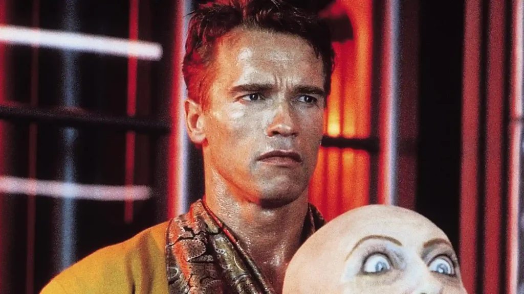 토탈리콜(1990) 스틸컷, 퀘이드(아놀드 슈워제네거)가 붉은 조명의 화성 장면에서 변장용 여성 마스크를 손에 들고 긴장된 표정을 짓고 있는 모습