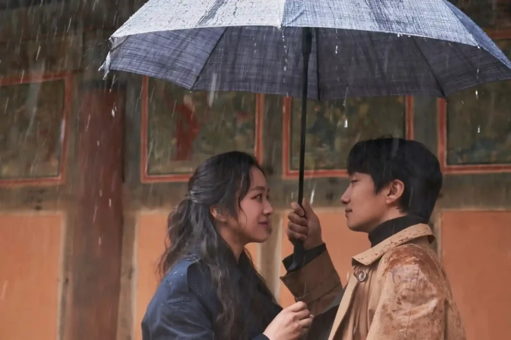헤어질 결심(2022) 스틸컷, 빗속에서 우산을 함께 쓴 서래(탕웨이)와 해준(박해일)이 서로를 바라보며 가까이 서 있는 장면
