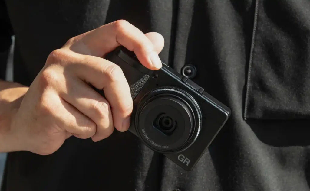 한 손으로 리코 GR 카메라를 쥐고 있는 모습, 검지가 셔터 위치에 자연스럽게 걸림