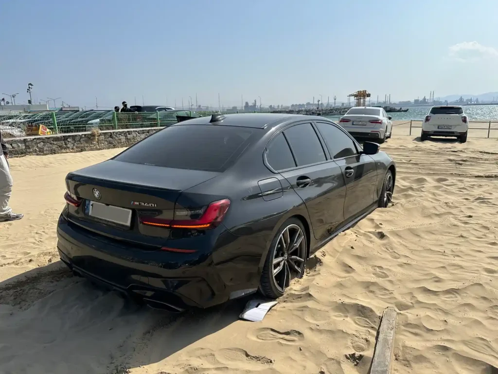 포항 영일대 공용주차장 모래에 매몰된 BMW M340i — 타이어 아래 박스를 깔아 인력 탈출을 시도하는 모습