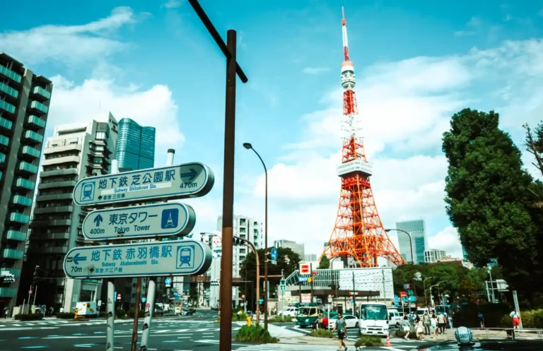 도쿄타워 방향 도로 표지판과 붉은 철탑이 함께 담긴 도쿄 시내 교차로 풍경