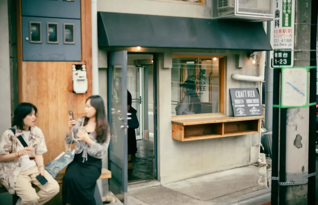 나카메구로 Sidewalk Coffee 입구 앞 벤치에 두 여성이 나란히 앉아 있고, 오른쪽 벽에 CRAFT BEER 칠판이 걸린 작은 카페 외관