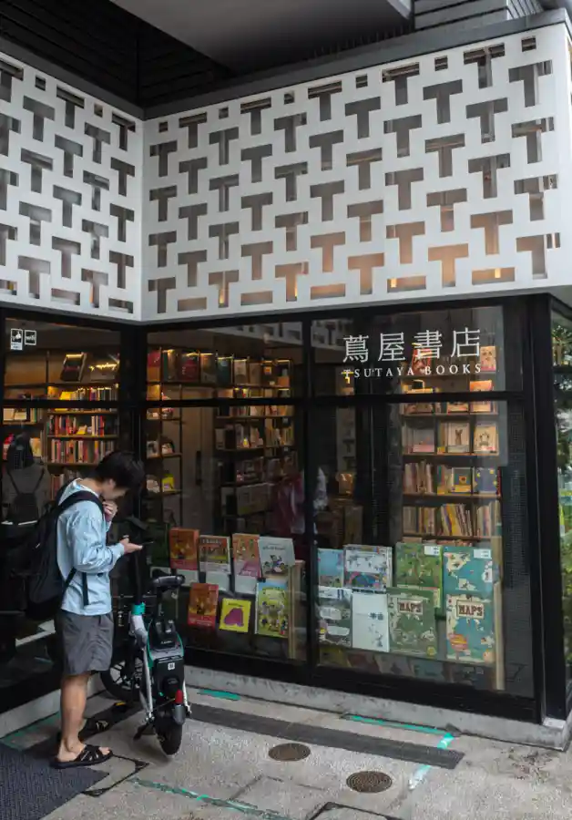 나카메구로 츠타야 서점 외관, T자 격자 패턴 외벽 아래 쇼윈도에 아동 서적이 진열되어 있고 앞에 킥보드를 세운 남성이 서 있는 모습