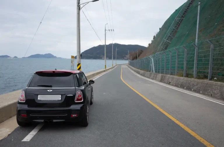 욕지도 해안일주도로 위에 세워진 검정 미니쿠퍼, 왼쪽으로 한려수도 바다와 섬들이 펼쳐지는 드라이브 코스 전경