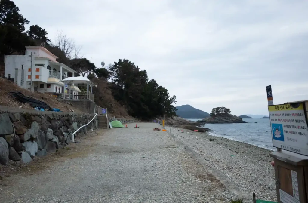 욕지도 흰작살해수욕장 전경, 몽돌 해변과 비탈에 자리 잡은 건물, 바다 너머 작은 섬이 보이는 겨울 풍경