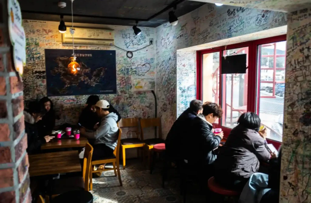 욕지도 할매바리스타 내부 — 방문객 글씨로 가득 찬 벽과 창가 자리에 앉은 손님들