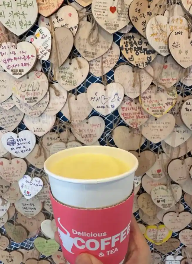 욕지도 할매바리스타 고구마라떼 — 하트 모양 나무패 배경 앞에서 든 고구마라떼 컵