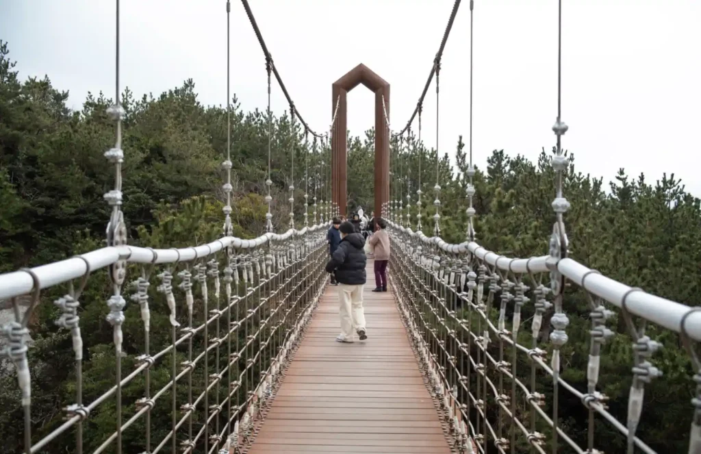 욕지도 제1출렁다리 위에서 바라본 정면 풍경, 흰색 와이어와 나무 데크로 이루어진 현수교 위를 관광객들이 걷고 있는 모습