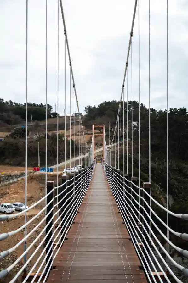 욕지도 제2출렁다리 위에서 바라본 정면 풍경, 흰색 와이어와 나무 데크로 이어진 현수교 너머로 고래강정 카페와 주차장이 보이는 겨울 풍경