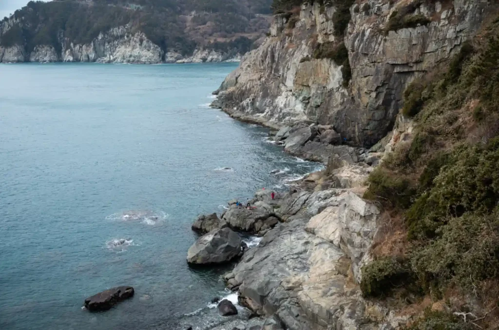욕지도 출렁다리 위에서 내려다본 해안 절벽과 갯바위 풍경, 절벽 아래 바위에 낚시하는 사람들이 보이는 겨울 한려수도 해안 전경