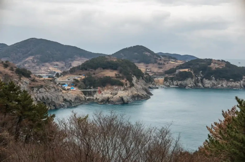 욕지도 비렁길 해안선 전경, 멀리 제3출렁다리 붉은 기둥과 제2출렁다리가 함께 보이는 겨울 한려수도 파노라마 풍경