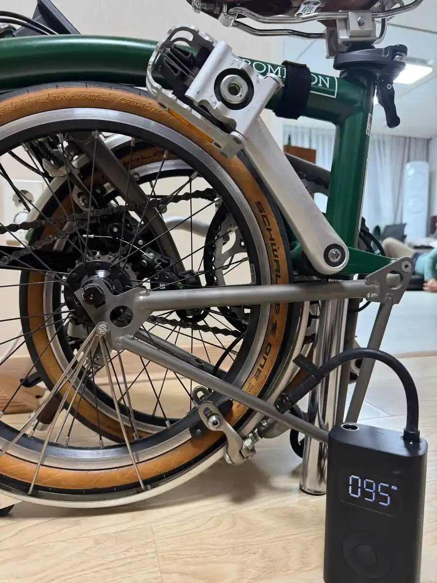 브롬톤 M4L 레이싱 그린 뒷바퀴에 전동 공기주입기를 연결한 모습 — 디스플레이에 95 PSI 표시