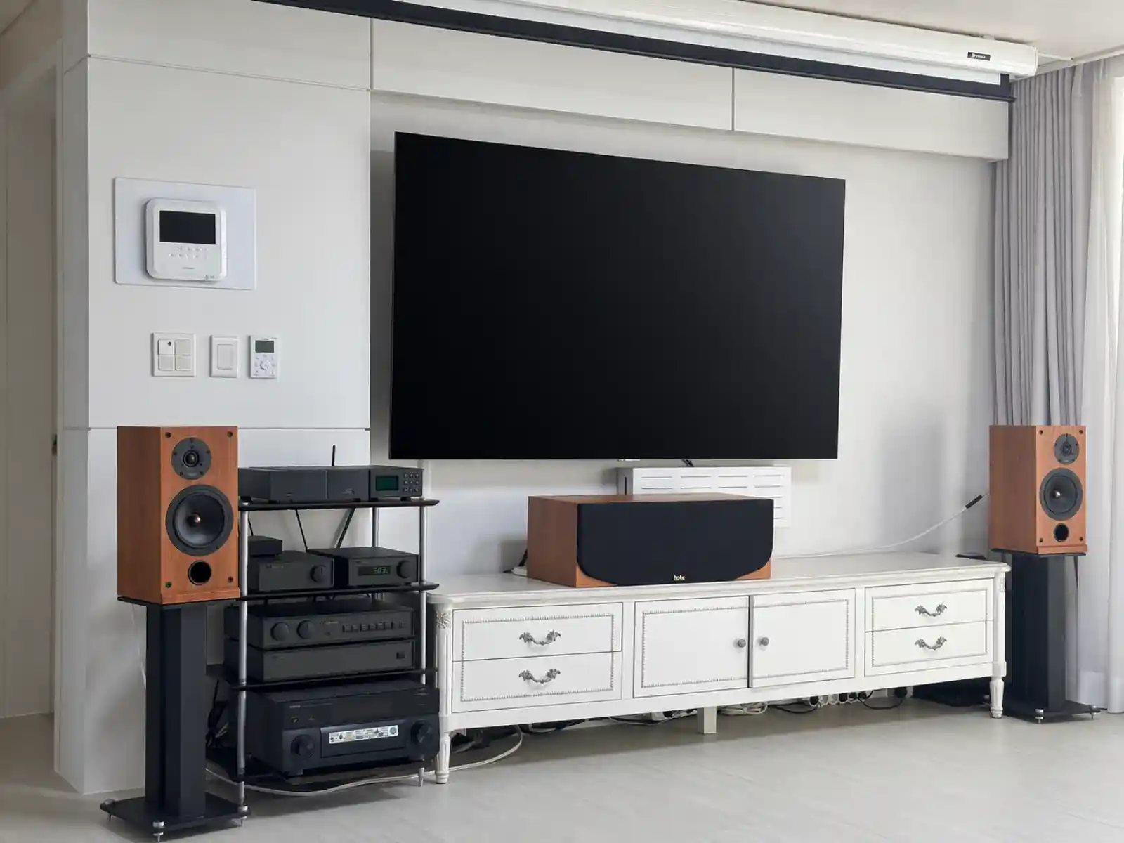 거실에 세팅된 Naim 시스템과 ProAc D2 스피커 전경. 블랙 랙에 NDX, nDAC, NAC 102, NAP 180이 적층되어 있고, 체리 우드 마감의 ProAc D2가 스탠드 위에 배치되어 있습니다.